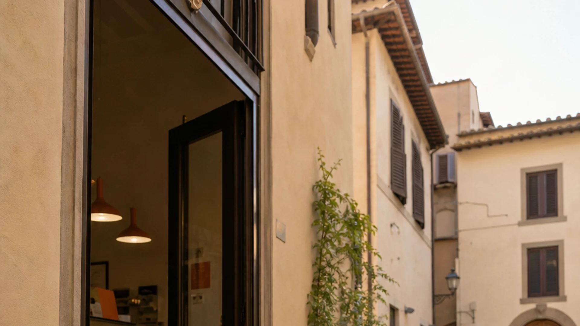 A photorealistic 16:9 scene of a small, sunlit Florentine piazza with cobblestones and terracotta-toned buildings, a compact gelato shop with an open doorway, locals sitting on steps eating gelato in paper cups, warm afternoon light casting long shadows. Alt: Gelateria della Passera in Piazza della Passera, a quiet local gelato spot in Florence's Oltrarno neighborhood.