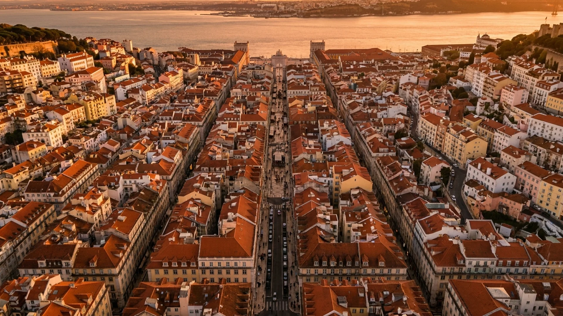 A photorealistic 16:9 aerial view of central Lisbon at golden hour, showing the terracotta rooftops, the Tagus River shimmering in the background, and the grid-like streets of Baixa meeting the hillside neighborhoods. Alt: Best neighborhoods to stay in Lisbon aerial overview at sunset.